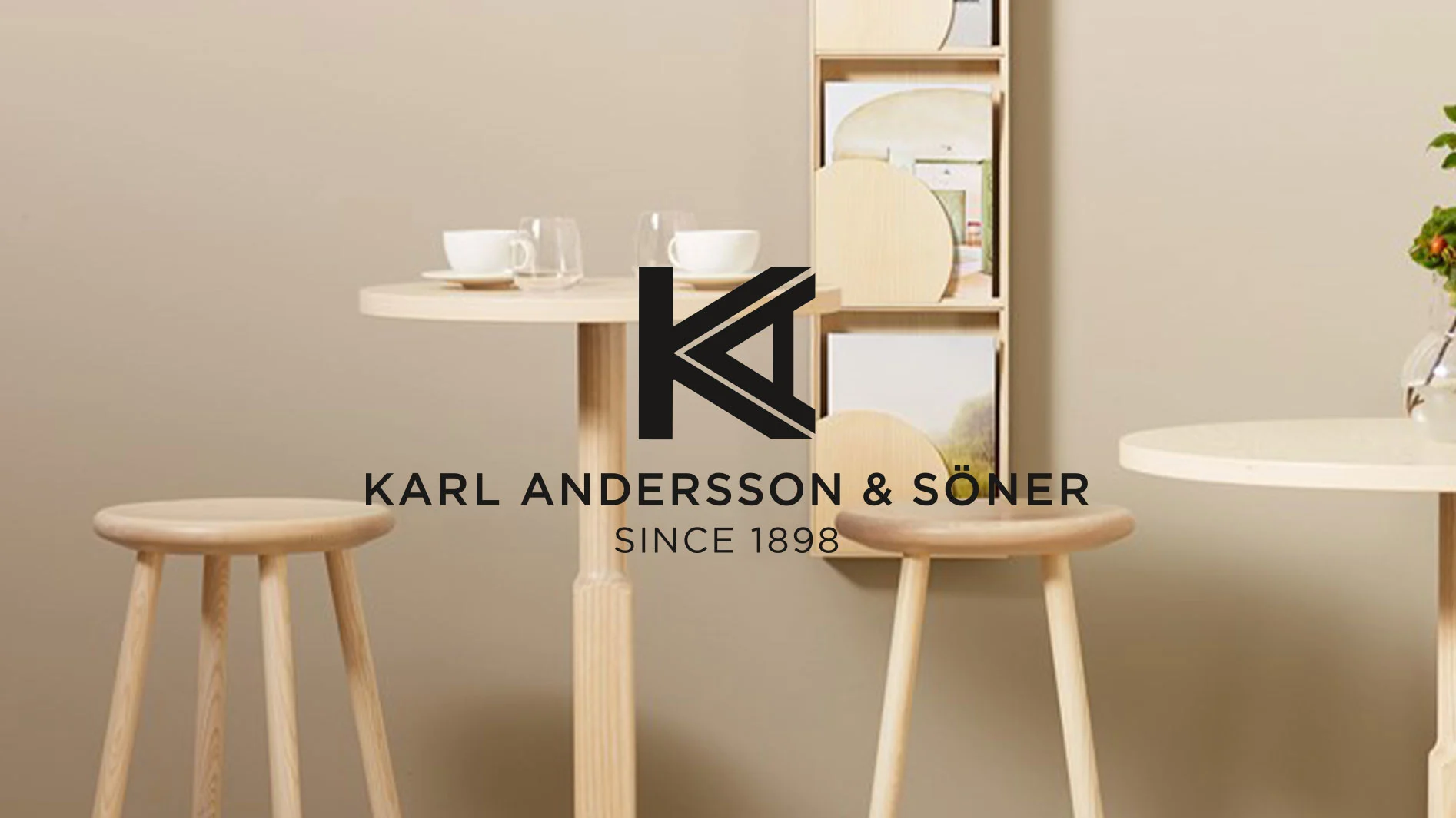 Tre ljusa träpallar och bord med en K-logotyp och texten Karl Andersson & Söner Since 1898 på ljusbrun bakgrund.