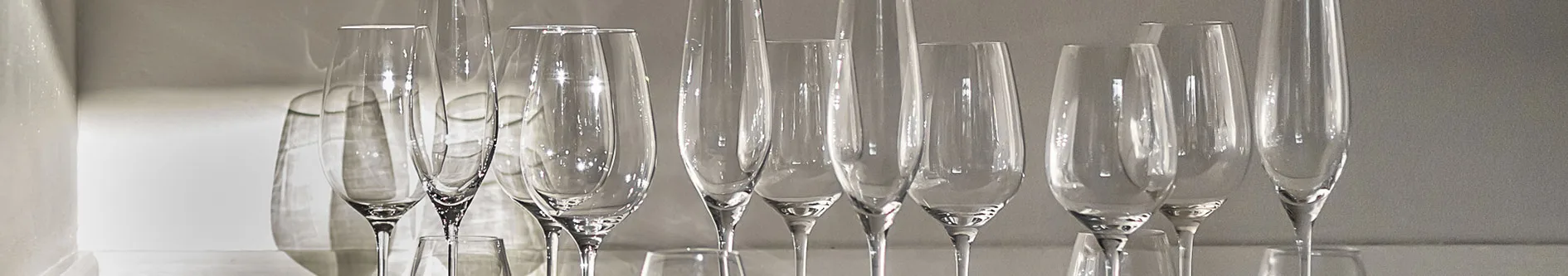 En rad med olika klara vinglas och champagneglas på fot på en ljus yta.