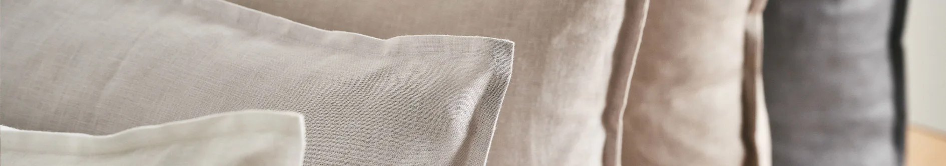 Närbild på lager av textilier i neutrala färger: ljusgrå, beige och mörkgrå.